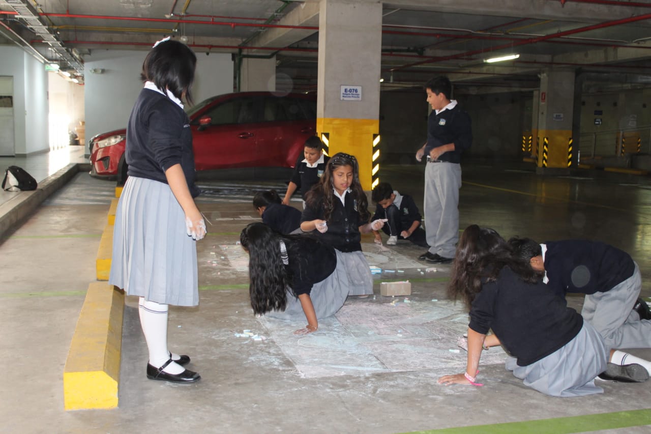 Un grupo de niños realizando una intervención artística en el suelo del Parqueadero de la Asamblea Nacional del Ecuador, acción enmarcada en la Muestra Arte Accesible, llevada a cabo en diciembre de 2019 en Quito, Ecuador.
