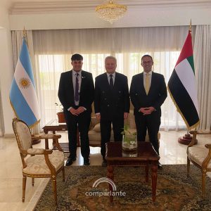 Fotografía donde Gerónimo se encuentra en la Embajada Argentina en los Emiratos Árabes junto a dos funcionarios públicos. Se encuentran vestidos de traje en un salón en medio entre una bandera argentina y una de Emiratos Árabes.