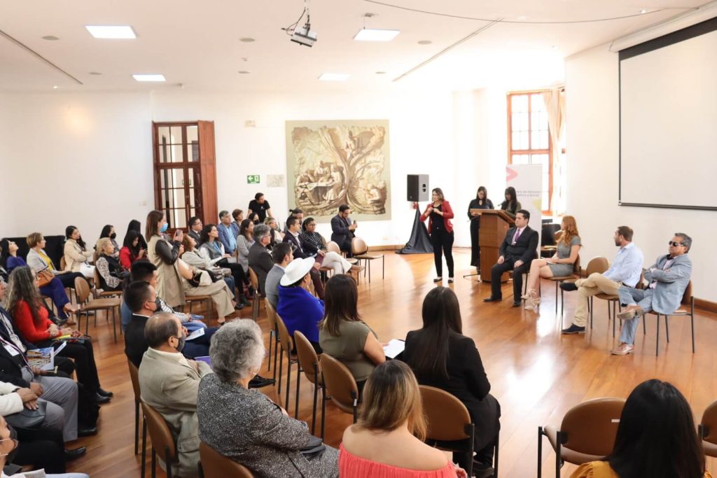 Photo of people visiting the exhibition touch with their hands a piece of art called "Legal Support 3". This piece of art consists of different constitutions piled up forming a tower of around 1,5 meters height.